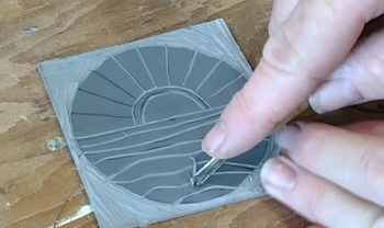 Using a chisel to cut the design into the linoleum block.
